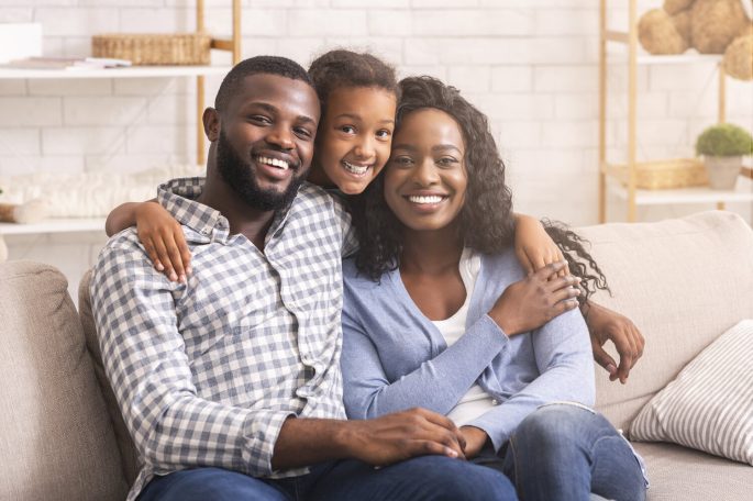 Family portrait. Happy african american parents and their daughter embracing and posing to camera while sitting together on couch at home